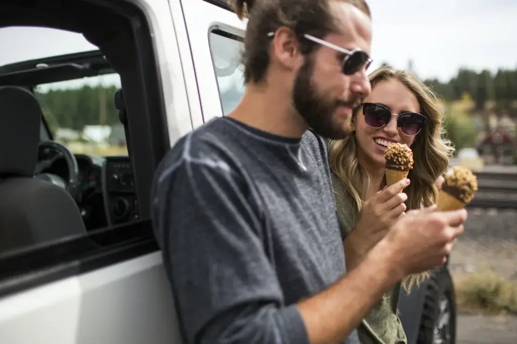 Young couple leaning against jeep eating ice cream cones