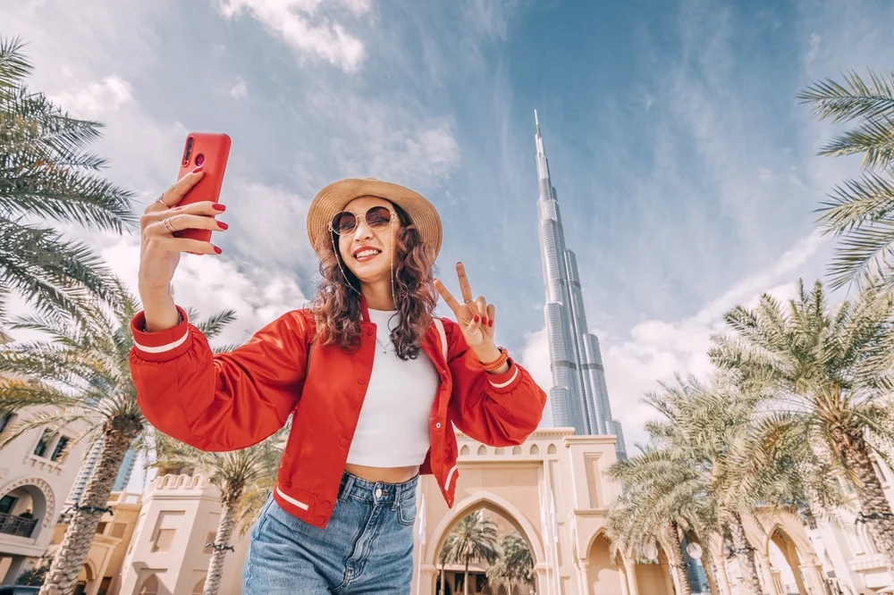 happy digital nomad asian girl taking selfie photos for her travel blog, in Dubai downtown by using apps for digital nomads.
