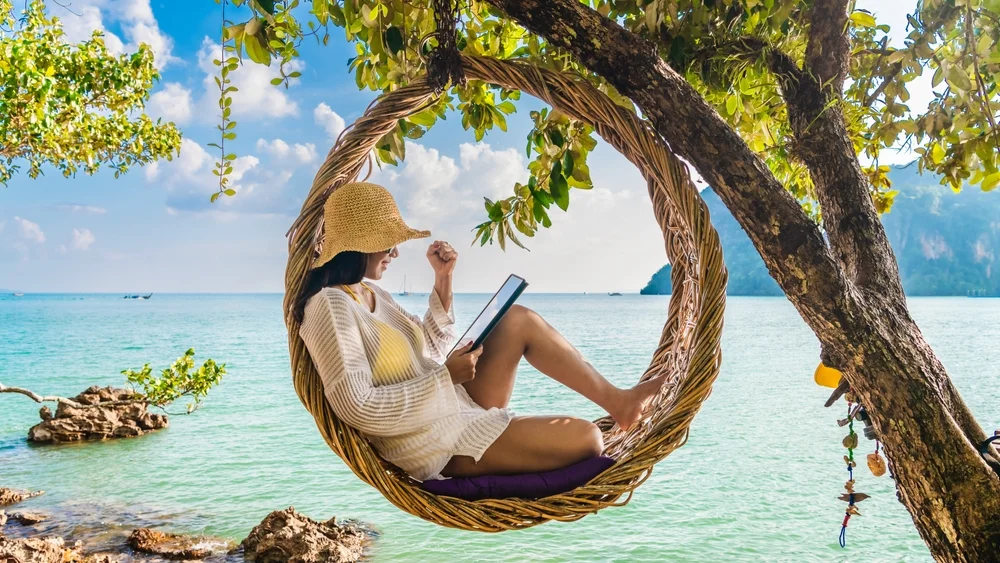 Digital nomad woman relaxing on straw nests using tablet at Railay beach Krabi, Asia business people on vacation at resort work with computer notebook, Tourist travel Phuket Thailand summer holiday trip
