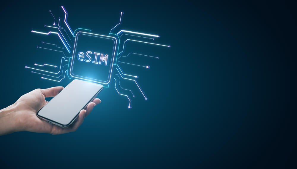 Close up of female hand holding cellphone with creative glowing eSim hologram on blurry background with mock up place. Embedded sim and cellular mobile technology concept
