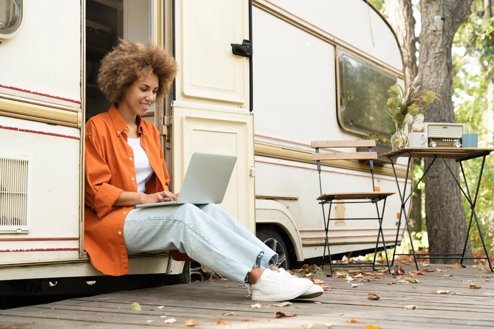 Young woman freelancer businesswoman working typing remotely on laptop computer with a caravan wifi while traveling alone in van camper home motor home trailer. E-learning concept
