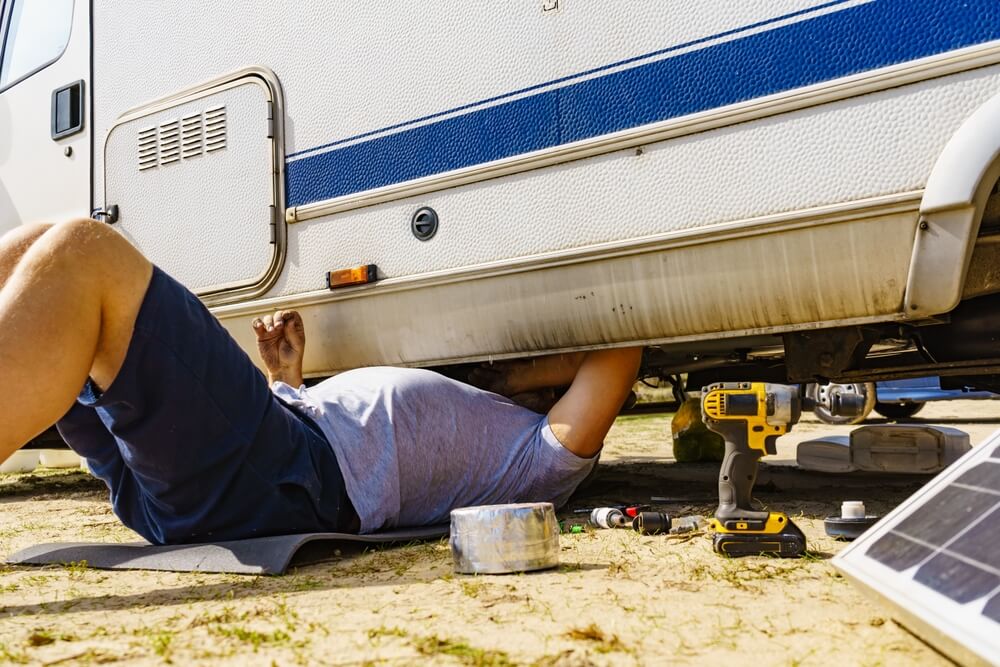 Man lying on ground, repairing bottom of the caravan vehicle. vanlife essentials
