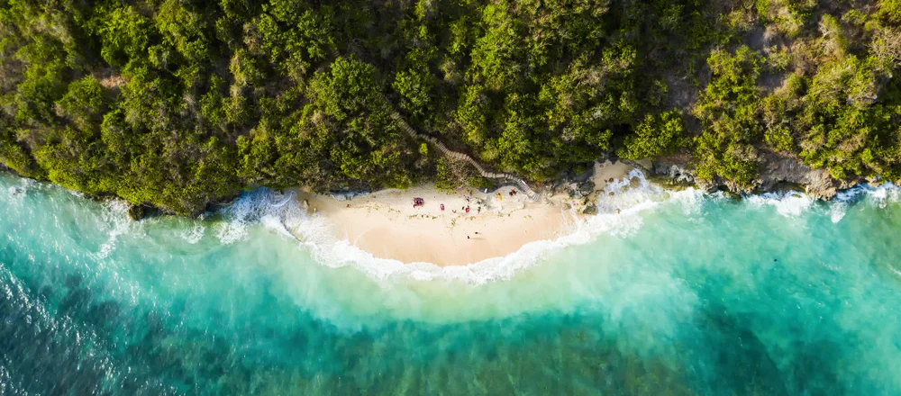 View from above, stunning aerial view of some tourists sunbathing on a beautiful beach bathed by a turquoise rough sea during sunset, Green Bowl Beach, South Bali, Indonesia.
