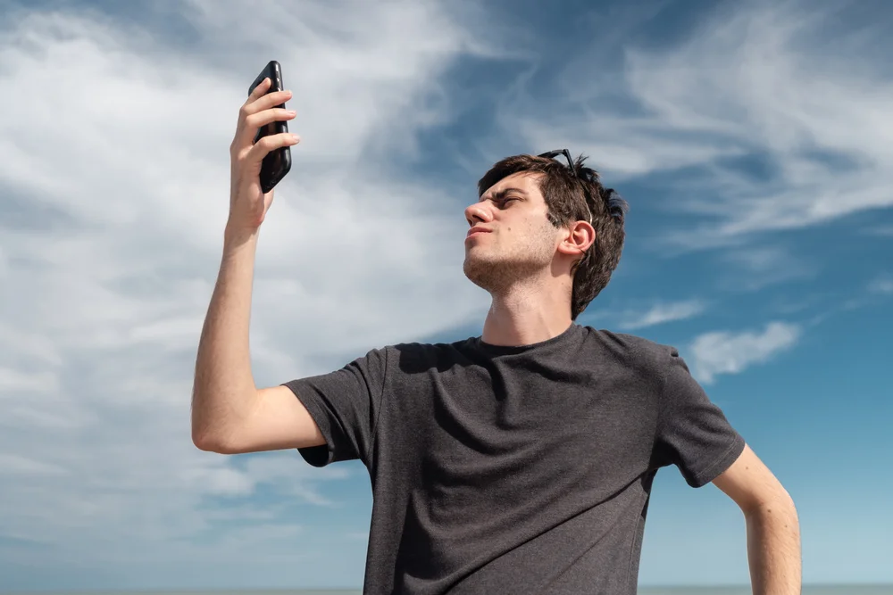 Low angle view of a young man searching for signal on his smartphone. Concept of connectivity and connection problems.
