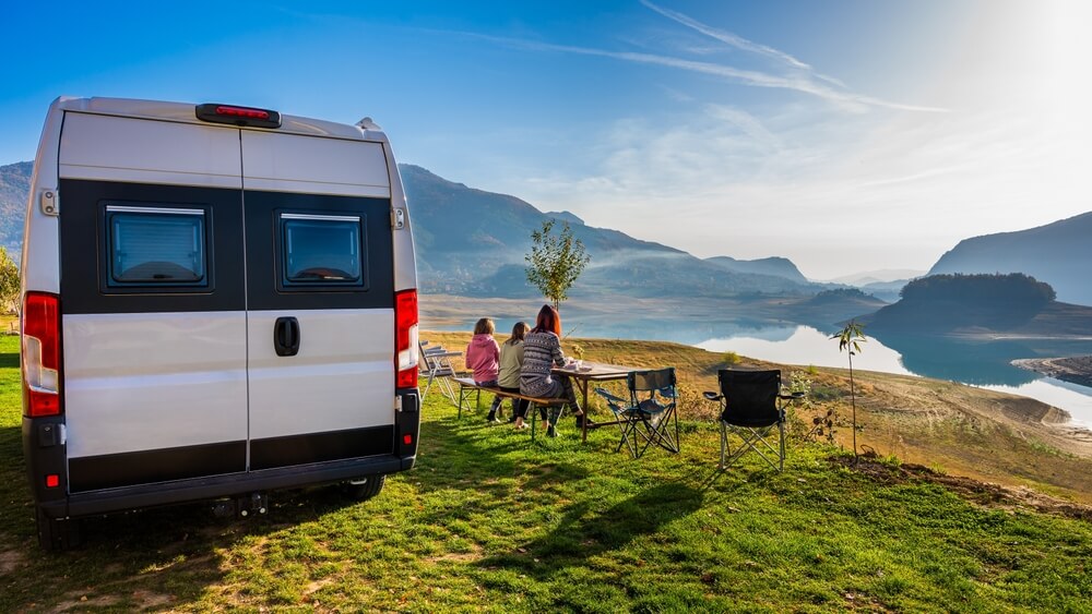 Campervan, Motorhome RV parked next to the lake or river in Bosnia and Herzegovina. Family with camper van or motor home eating breakfast on an active family vacation on a road trip to Ramsko lake.
