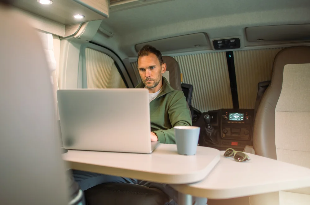 Caucasian Men in His 40s Working on His Computer Straight stream From His Camper Van While on a Road Trip. Remote Working Theme.
