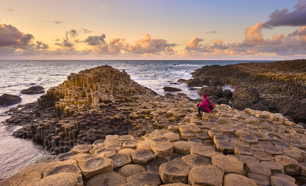 woman admiring sunset between Volcanic hexagonal basalt columns of Giant`s Causeway in Northern Ireland
