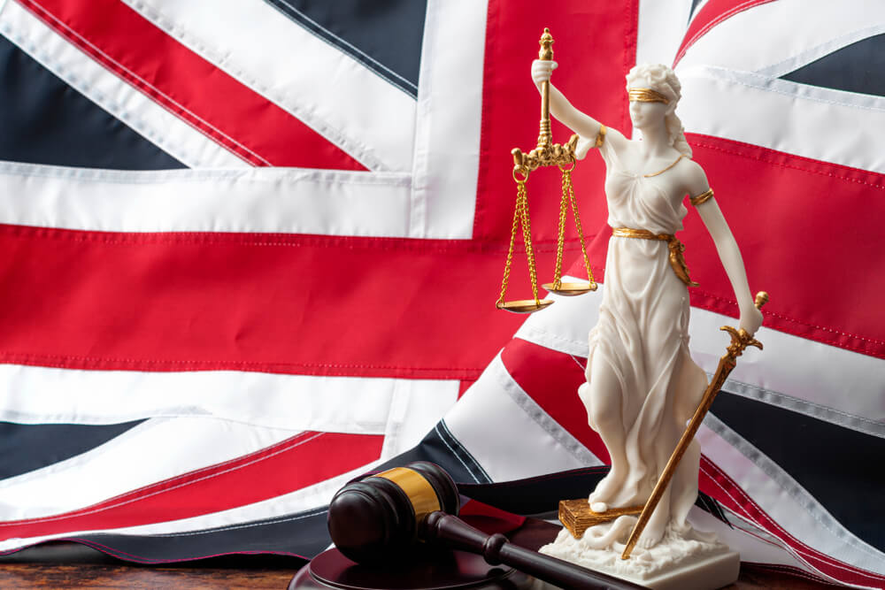 Social contract and the rule of law in the United Kingdom of Great Britain concept theme with statue of goddess Justitia, wooden gavel and the UK flag or the Union Jack in background with copy space
