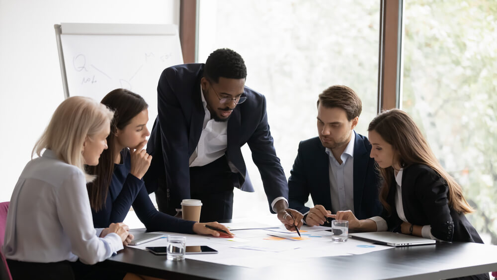 Confident african American male boss work cooperate with diverse team at office briefing, focused biracial businessman head meeting, collaborate discuss business ideas with colleagues at meeting
