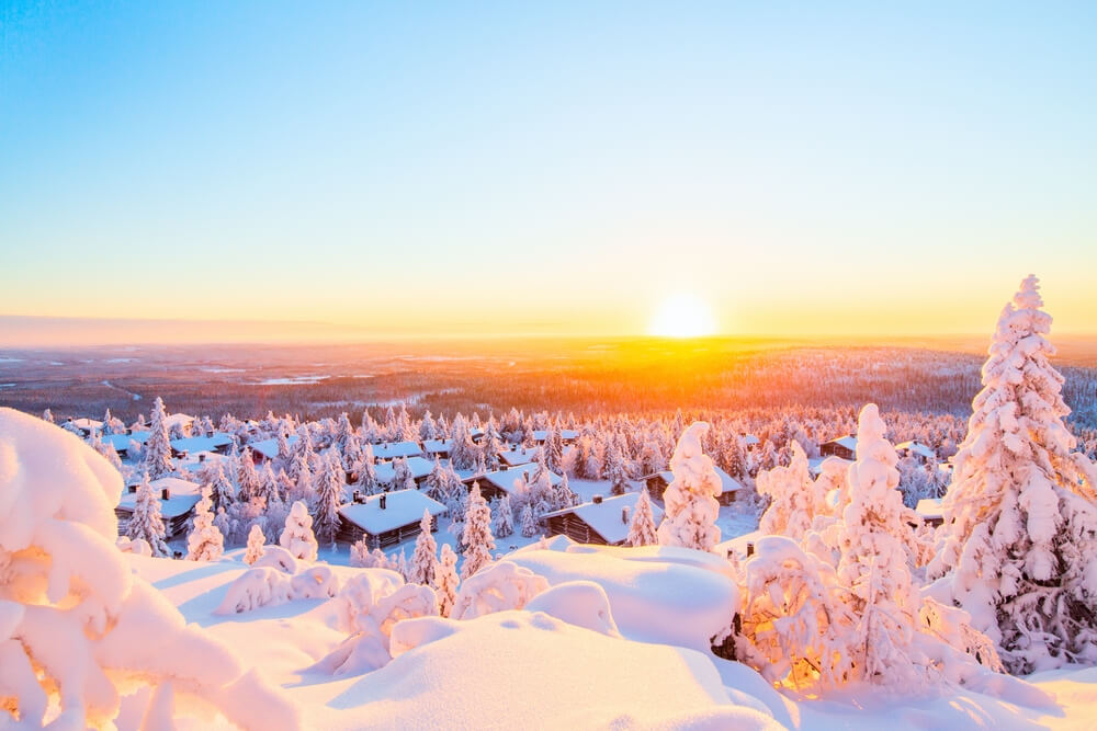 Stunning sunset view over wooden huts and snow covered trees in Swedish Lapland

