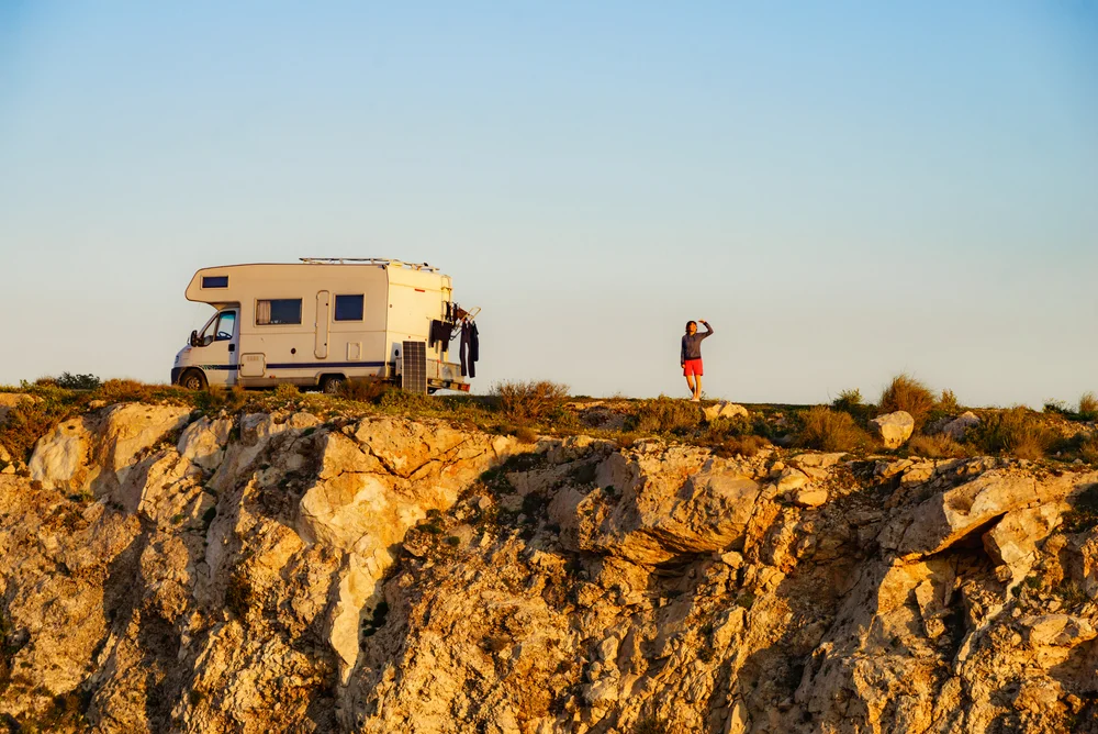 Female traveling with motor home. Camper vehicle wild camping on cliff rock, Cabo de Gata Nijar Natural Park in Almeria province, Andalusia Spain.
