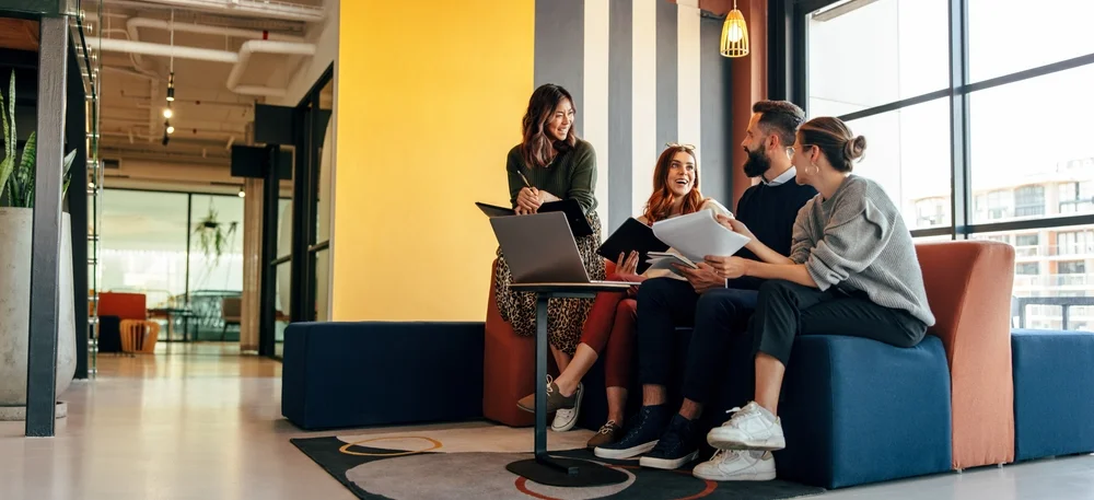 Multicultural businesspeople working in an office lobby. Group of happy businesspeople smiling while sitting together in a co-working mnomadism space. Young entrepreneurs collaborating on a new project.
