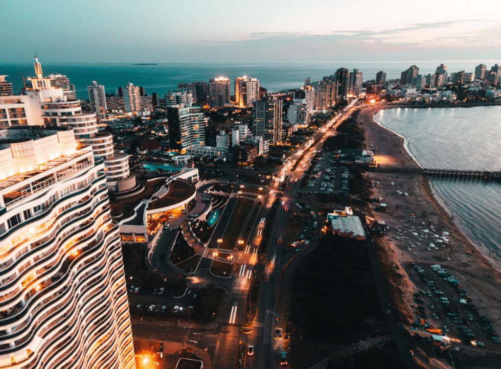 Aerial view of Punta del Este, Uruguay at sunset featuring modern high-rise buildings, illuminated coastal roads, and the beachfront by the Atlantic Ocean