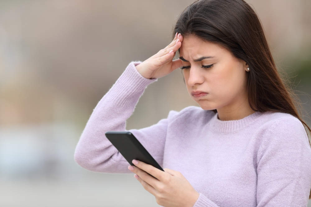 Frustrated teen checking smart phone content standing in the street
