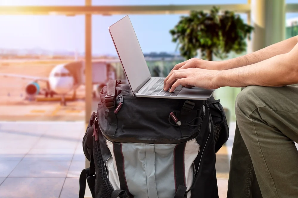 Cropped shot of an unrecognizable digital nomad sitting alone and typing on his laptop during the day at airport with digital nomad essentials

