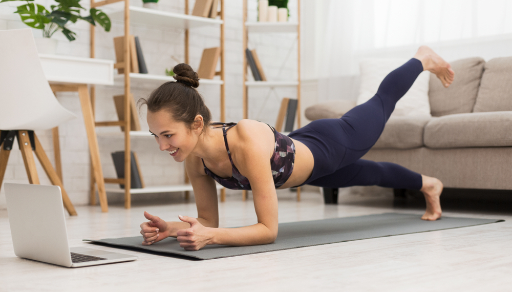 Fit woman doing yoga plank and watching online tutorials on laptop, training in living room
