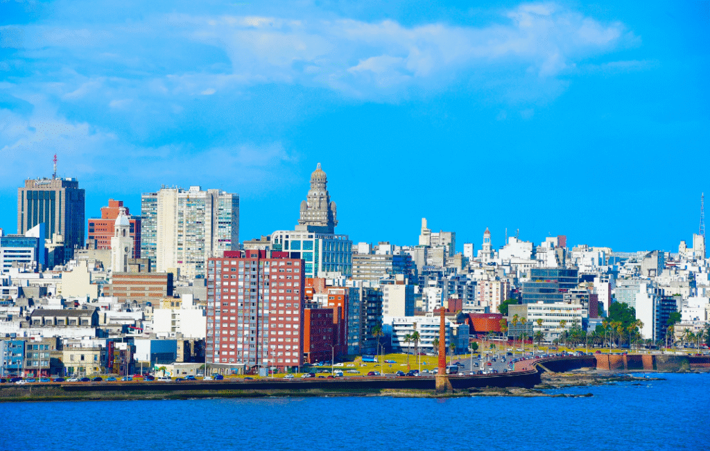 Daytime cityscape of Montevideo, Uruguay with the iconic Palacio Salvo and diverse skyline along the Rambla coastline under a vibrant blue sky.
