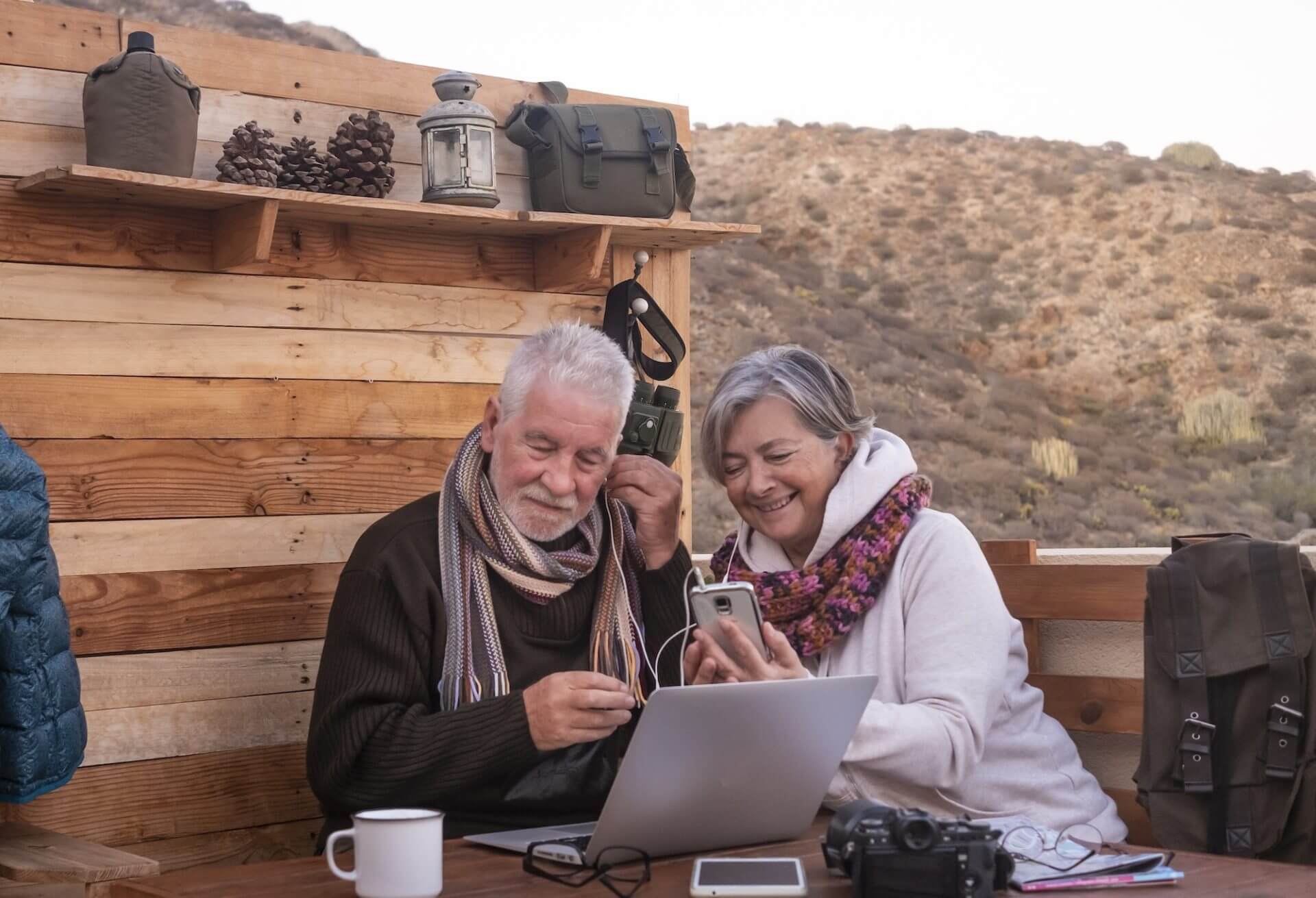 Senior couple pauses at rustic mountain bar before continuing the hike. Nomadic people with laptop