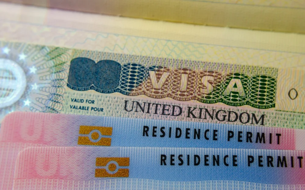 United Kingdom BRP (Biometrical Residence Permit) cards for Tier 2 work visa placed on top of UK VISA sticker in the passport. Close up photo.
