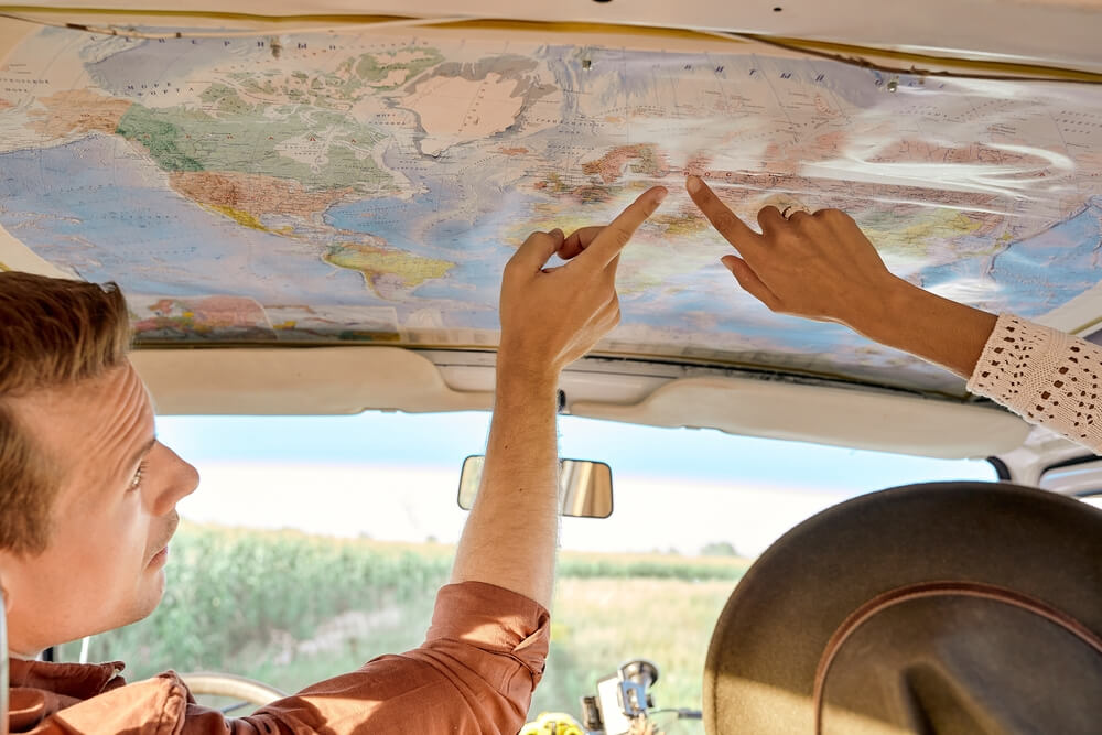 Summer trip concept. cropped friends or couple looking at map to plan a camper van trip pointing finger at map. rear view, view from back. vacation, holidays, adventure, journey, trip, travel
