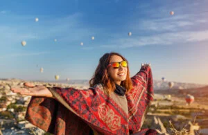 A tourist girl on a mountain top enjoying wonderful view of the sunrise and balloons in Cappadocia. Happy Visit Turkey concept