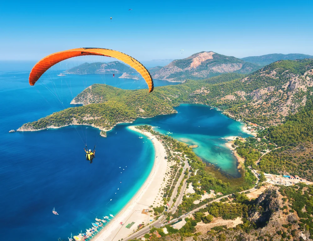 Paragliding in the sky. Paraglider tandem flying over the sea with blue water and mountains in bright sunny day. Aerial view of paraglider and Blue Lagoon in Oludeniz, Visit Turkey. Extreme sport. Landscape
